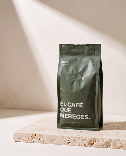 Bolsa verde de CIMA Reserva de 500 g sobre una losa de travertino, contra un muro claro cruzado por una diagonal de luz