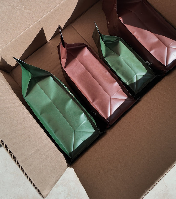Foto real: bolsas de CIMA Reserva y CIMA Origen de 250 g dentro de la caja de envío abierta, vistas desde arriba