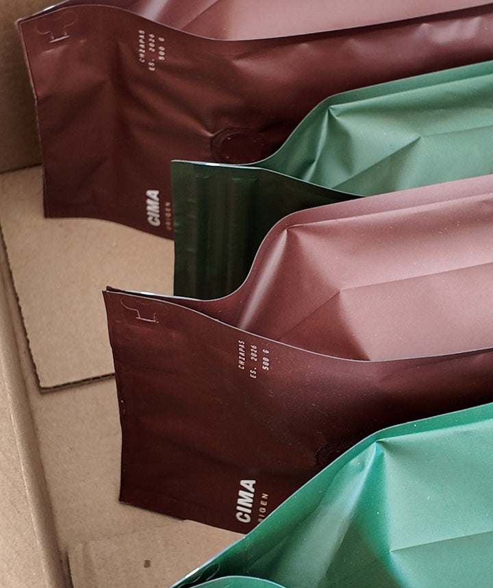 Foto real: bolsas de CIMA Origen y CIMA Reserva de 500 g en su caja de envío, vistas de costado