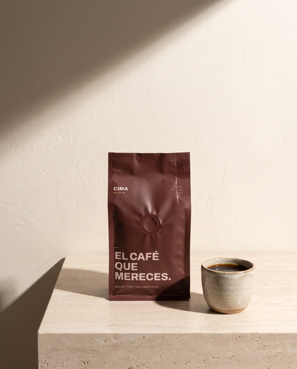 Bolsa vino de CIMA Origen de 250 g sobre una repisa de travertino, junto a una taza de barro con café