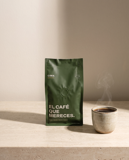 Bolsa verde de CIMA Reserva de 250 g sobre una repisa de travertino, junto a una taza de barro con café recién servido
