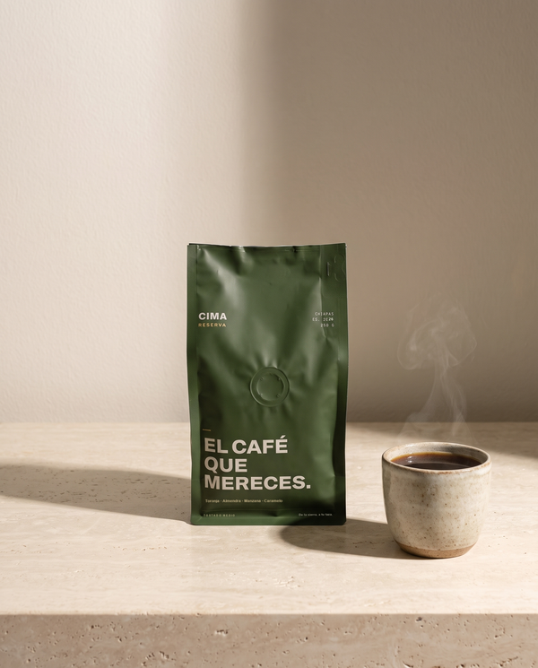 Bolsa verde de CIMA Reserva de 250 g sobre una repisa de travertino, junto a una taza de barro con café recién servido